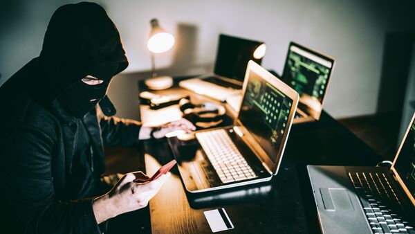 Computer hacker sitting in front of laptop late at night and using phone