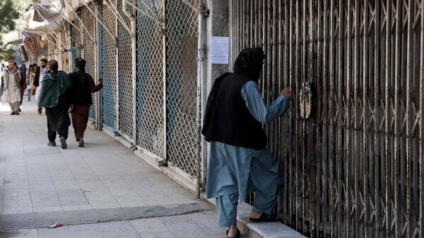 Afghan men walk past shops closed in solidarity with victims killed in an attack by unidentified armed men on the outskirts of the Sayed Mohammad Agha Shia shrine, a day after the incident in Herat on April 11, 2026.