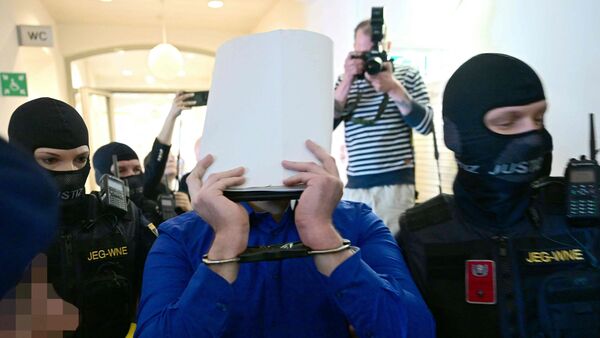 A defendant in handcuffs is escorted to the courtroom by justice officers as a trial starts at court in Wiener Neustadt, Austria, on April 28, 2026, over a plot to attack a Taylor Swift concert in Vienna. The main suspect, who has been in detention since his arrest in August 2024, is facing terror offenses and other charges, prosecutors said.