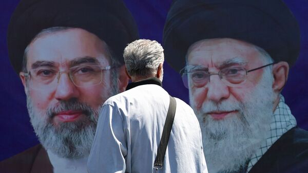 A man walks past a banner with pictures of Iran's slain supreme leader Ayatollah Ali Khamenei (R) and his son and successor Mojtaba Khamenei, installed along a street in Tehran on April 15, 2026. The United States has not formally agreed to extend its two-week ceasefire with Iran, a senior official said on April 15, after reports that President Donald Trump's administration had consented in principle to lengthen the truce. (Photo by AFP) /