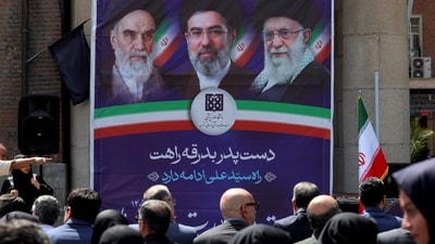 People sit before a banner depicting Iran's supreme leaders since 1979: Ayatollahs Ruhollah Khomeini (L, until 1989), Ali Khamenei (R, until February 2026), and Mojtaba Khamenei (C, incumbent) during a rally condemning attacks on health facilities by the US and Israel outside at Imam Khomeini Hospital in Tehran. (Photo by AFP) (AFP)