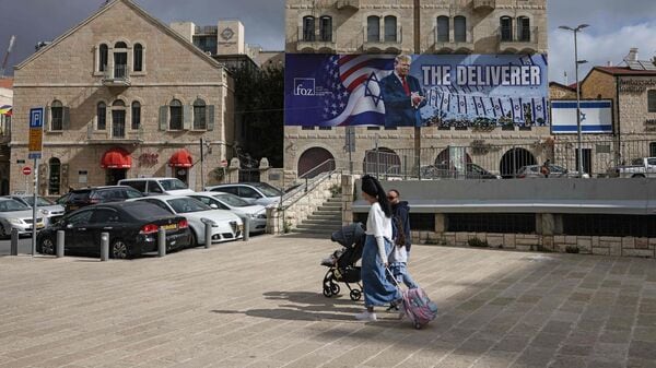 People walk past a banner depicting US President Donald Trump with the slogan �The Deliverer� in Jerusalem on April 20, 2026. Iran is not currently planning to attend talks with the United States, state media said, after the US president ordered US negotiators to travel to Pakistan on April 20, just days before a ceasefire in the Middle East expires. (Photo by AHMAD GHARABLI / AFP) /