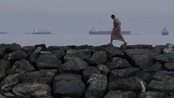 FILE- A man walks along the shore as oil tankers and cargo ships line up in the Strait of Hormuz, seen from Khor Fakkan, United Arab Emirates