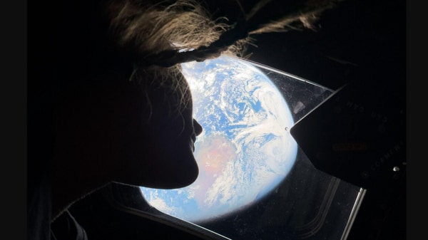 NASA astronaut and Artemis II mission specialist Christina Koch peers out of one of the Orion spacecraft's main cabin windows, looking back at Earth, as the crew travels towards the Moon