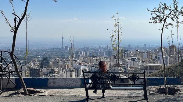 A woman sits on a bench overlooking the city at Pardisan Park in Tehran on April 22, 2026. The US president extended a ceasefire with Iran to allow more time for talks, claiming the Islamic republic was 'collapsing financially' because of the blockade of the Strait of Hormuz. (Photo by AFP)