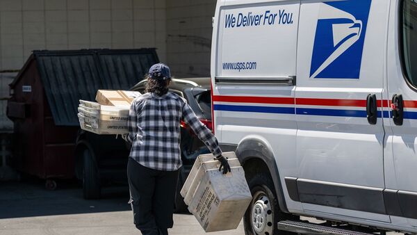 A United States Postal Service (USPS) worker carries containers and packages from a vehicle in Tracy, California, US.