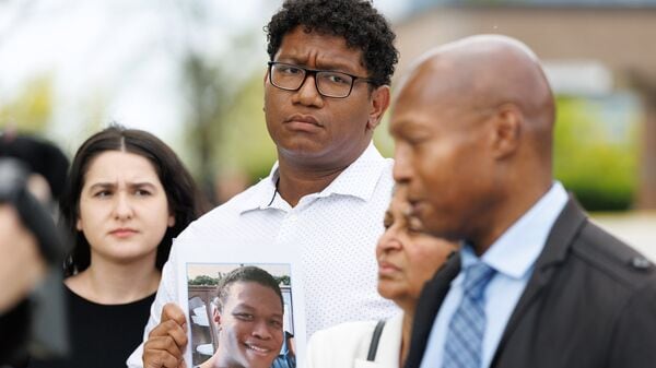 Ethan Mitchell holds a photograph of his brother, Stephen Mitchell Jr., as his partner Elena Castors, left, stands beside him as Stephen Mitchell, right, speaks to the media with Latha Mitchell, outside the Ontario Court of Justice, Friday, May 29, 2026, in Newmarket, Ontario, (The Canadian Press via AP)