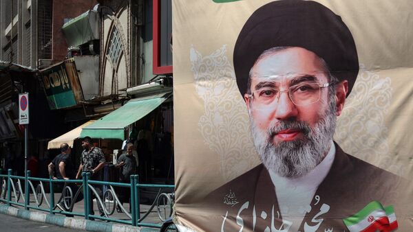 Iranians stand on a pavement along a street next to a billboard depicting Iran's Supreme Leader Ayatollah Mojtaba Khamenei, in Tehran on April 24, 2026. (Photo by AFP)