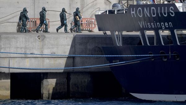 Persons wearing protective suits walk toward the hantavirus-stricken cruise ship MV Hondius docked in the port of Granadilla de Abona on the island of Tenerife in Spain's Canary Islands on May 11, 2026. (Photo by JORGE GUERRERO / AFP)