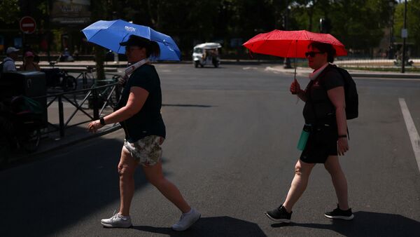 People cross the road whilst taking shelter under umbrellas in central Paris during high temperatures amid a heatwave in Paris, France, June 27, 2026. REUTERS/Tom Nicholson