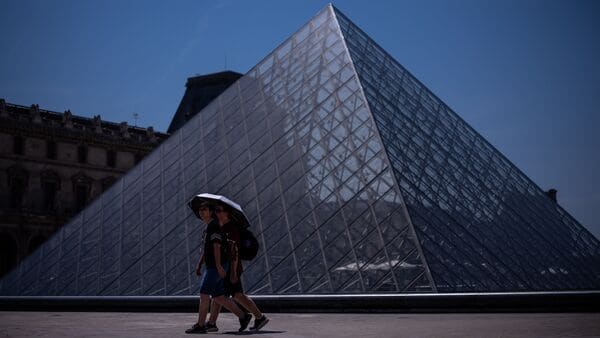 Tourists with an umbrella walk near the Louvre museum during a heat wave in Paris.