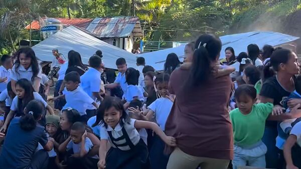 This frame grab made from UGC video footage courtesy of Deped Mahayahay Elementary School shows huddled schoolchildren in a field reacting as a structure (background) collapses during an 7.8 magnitude earthquake in Malita town, Davao del Sur province on June 8, 2026.
