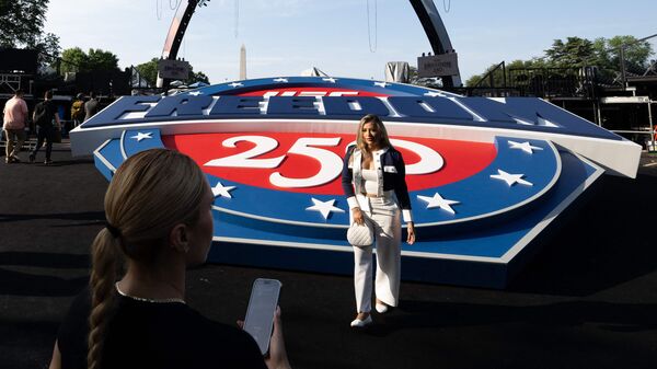A woman poses by a UFC Freedom 250 logo and the structure, known as The Claw, for the UFC fight that US President Donald Trump hosted as part of the 250th anniversary of the United States is seen on the South Lawn of the White House during a media preview in Washington, DC, June 11, 2026. (Photo by SAUL LOEB / AFP)