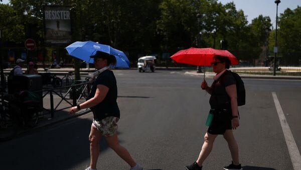 People shield themselves with umbrellas while crossing a road. The National Weather Service in the US says that most parts of America could experience a heatwave this week.