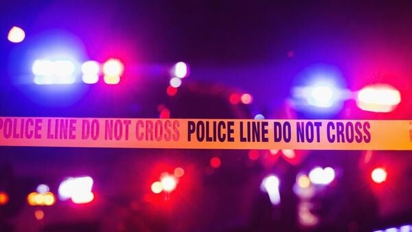 Accident or crime scene cordon tape, police line do not cross. It is nighttime, emergency lights of police cars flashing blue, red and white in the background (Getty Images/iStockphoto)