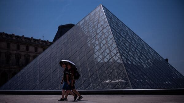 Tourists with an umbrella walk near the Louvre Museum in Paris