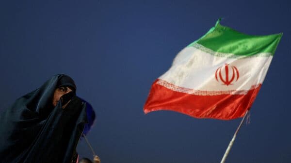 An Iranian woman prays near an Iranian flag, as preparations are underway ahead of a farewell ceremony for Iran's late Supreme Leader Ayatollah Ali Khamenei, at Enghelab Square in Tehran, Iran, July 2, 2026.