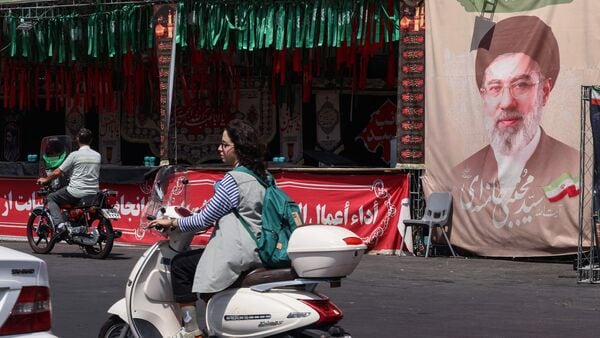 A woman rides a motorcycle past a banner of Iran's Supreme Leader Mojtaba Khamenei at Valiasr Square in Tehran on July 19, 2026 | Representational image
