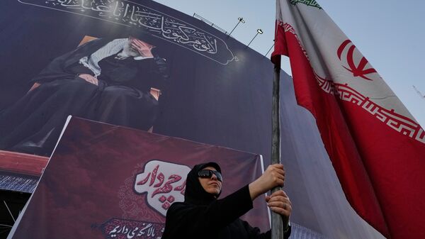 US-Iran War News Live: A pro-government woman holds an Iranian flag under a banner showing a portrait of the slain Supreme Leader Ayatollah Ali Khamenei, who was killed during the U.S. and Israel strike on Feb. 28, at a square in downtown Tehran.