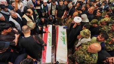 Mourners gather around the coffins of Popular Mobilization Forces fighters as a child rests on one of them during the funeral of those killed in airstrikes on PMF bases in Najaf, Iraq on Thursday