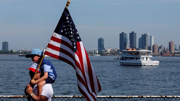 A man carries a boy piggyback, who holds onto a US flag, during a helicopter flyover, at the start of the Sail 250 parade of ships, as the United States celebrates its 250th anniversary on Independence Day in New York City.