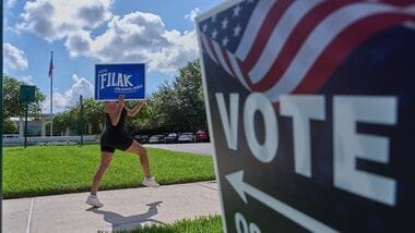 Yvette Allen, of Celebration, Fla., exercises while holding up a sign for a local school board election outside of the West Osceola Branch Library, during early voting for the Florida primary election, in Celebration, Fla., Thursday, Aug. 13, 2026. (AP Photo/Jacquelyn Martin)