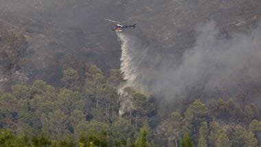 Greek wildfires have claimed five lives, including two pilots who died in a helicopter collision while battling blazes near Athens.