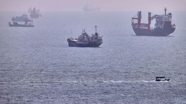 A small boat sails past cargo ships and other commercial vessels anchored in the Strait of Hormuz off Bandar Abbas, Iran, Wednesday, Aug. 5, 2026.