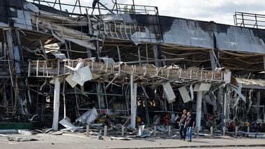 Latest news on August 16, 2026: Men walk outside a burnt-out hypermarket following an overnight attack, what Russian-installed authorities called a Ukrainian drone strike, in the course of the Russia-Ukraine conflict in Yenakiieve (Yenakiyevo) in the Donetsk region, a Russian controlled area of Ukraine, August 14, 2026.