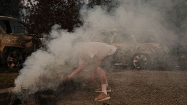 Pete Reuter throws gravel to smother a smoking piece of wood at a neighbor's house after a wildfire hit the northern part of Spokane, Wash., Monday, Aug. 3, 2026.